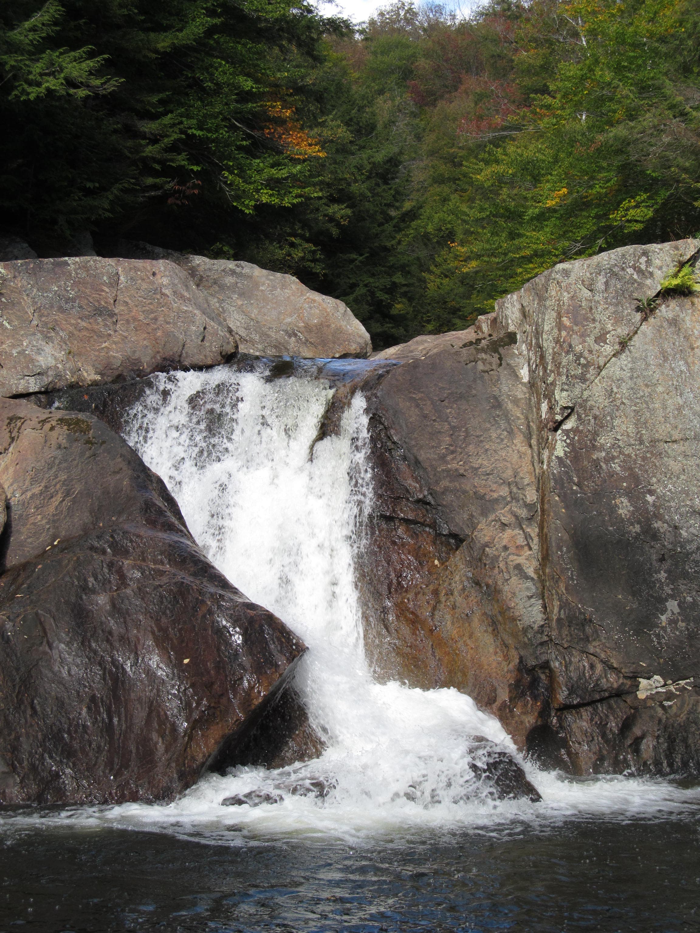 Close view of a vigorous cascade over dark wet boulders into foamy water at Buttermilk Falls, Ludlow, Vermont.